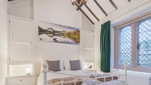 Un dormitorio con una cama blanca, una mesita de noche, un cuadro en la pared y una ventana con cortina.