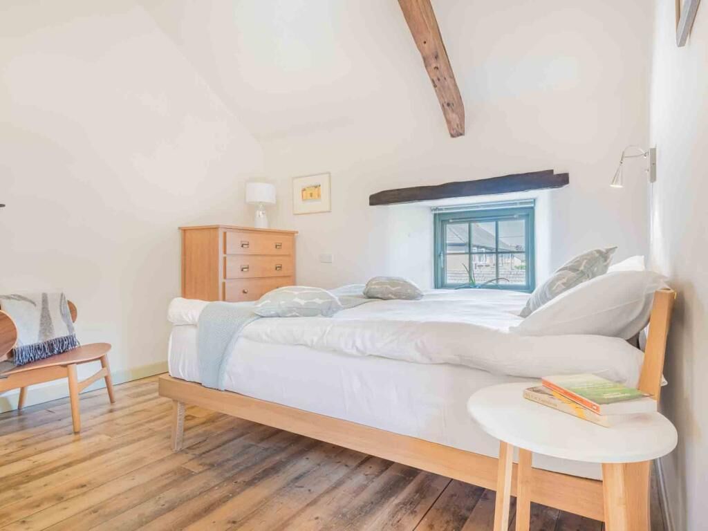 Une chambre à coucher avec un lit en bois, une petite table de chevet, une commode, une fenêtre donnant sur un beau paysage et une lampe.