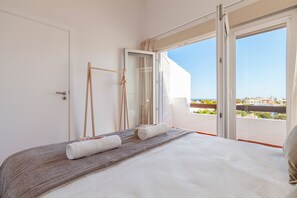 A bedroom with a bed, a window with a view of the city, and a door.