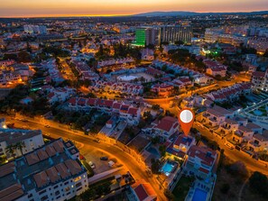 Vista aérea de un paisaje urbano al atardecer, con edificios, carreteras y un hotel destacado con piscina.