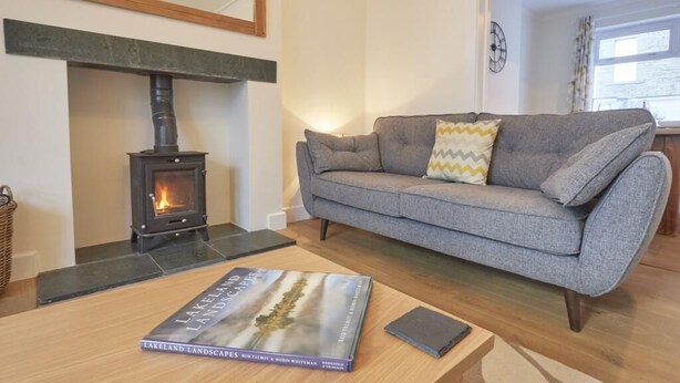 Een gezellige woonkamer met een bank, een boek getiteld 'Lakeland Landscapes' en een houtkachel.