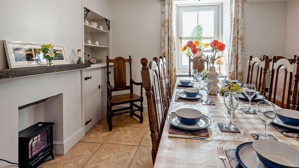 A dining room with a long table set for six, a fireplace, and a chandelier.