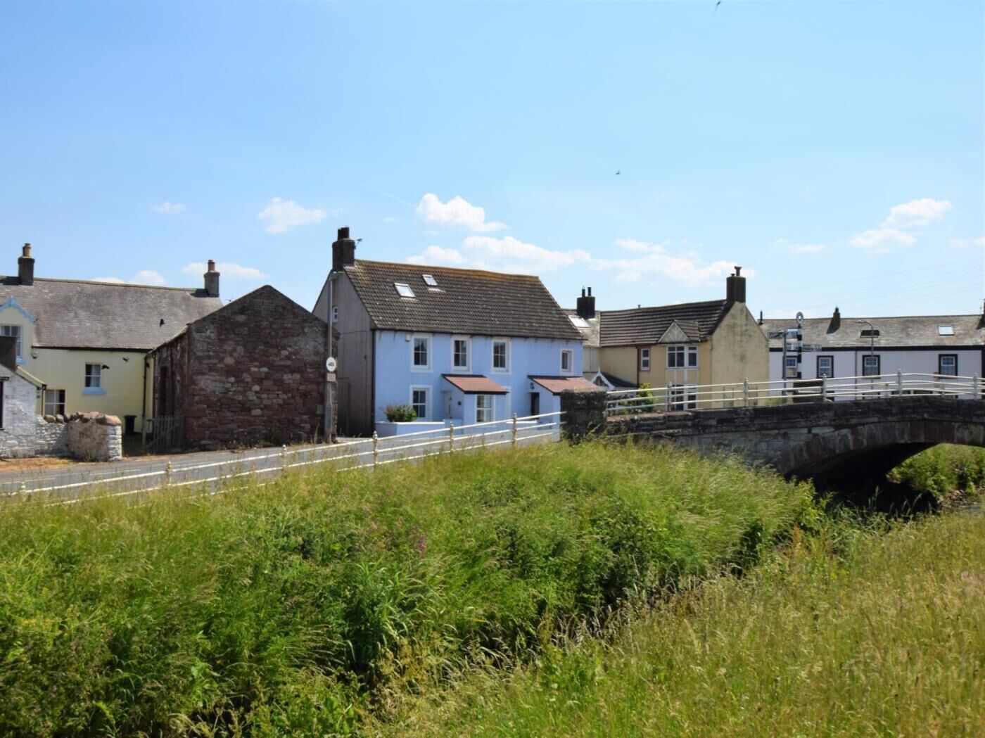 A rural bridge, stone buildings, and a grassy foreground.