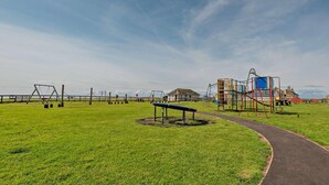 A playground with swings, a climbing structure, and a path leading to a building.