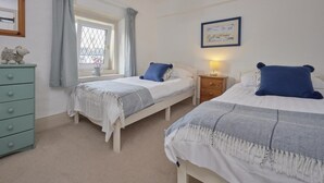 Une chambre avec deux lits simples, une commode, une fenêtre avec des rideaux, une lampe de chevet et un tableau encadré au mur.