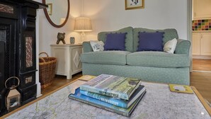 Un salon avec un canapé vert, une cheminée, un miroir et une pile de livres.