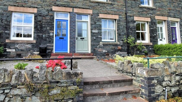 A stone building with multiple windows, a blue door, and a sign indicating 'Steps Keep Clear.' - 2 Bed in Keswick (oc-sz117) (Keswick)