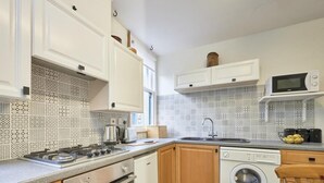 A kitchen with white cabinets, a microwave, a washing machine, and patterned backsplash tiles. - 2 Bed in Keswick (oc-sz117) (Keswick)