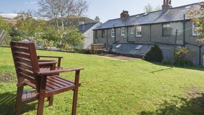 A grassy yard with a wooden bench, a stone building with a sloped roof, and a hill in the background. - 2 Bed in Keswick (oc-sz117) (Keswick)