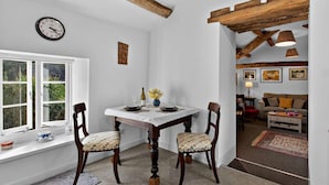 Un comedor con una mesa blanca, dos sillas, un reloj y una ventana con vistas a follaje.