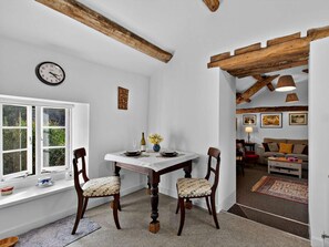 A dining area with a white table, two chairs, a clock, and a window with a view of greenery. - 1 Bed in Carnforth (oc-sz527) (Barbon)