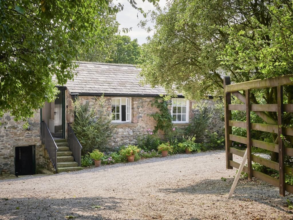 A stone building with a gravel driveway, wooden gate, and potted plants.