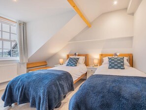 Ein Schlafzimmer mit zwei Betten, Holz-Kopfteilen, Nachttischen mit Lampen und einem Fenster mit Vorhängen.