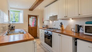 Una cocina con armarios blancos, encimera de madera, estufa, horno, lavabo y microondas.