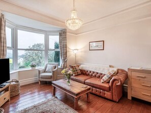 A living room with a leather sofa, a wooden coffee table, a television, and a chandelier. - 2 Bed in Holmrook (oc-sz464) (Irton with Santon)