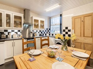 A modern kitchen with white cabinets, a black and white checkered backsplash, a stainless steel range hood, and a dining area with a wooden table set for two. - 2 Bed in Holmrook (oc-sz464) (Irton with Santon)