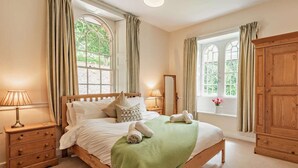 Ein Schlafzimmer mit einem hölzernen Bett, zwei Nachttischen, einem Schrank und großen Fenstern mit Vorhängen.