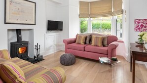 A living room with a sofa, a television, a fireplace, and a window with a view of greenery. - 2 Bed in Windermere (oc-sz306) (Windermere)