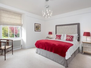 A bedroom with a large bed, a chair, a radiator, a window with a view, a bedside table, and a lamp. - 2 Bed in Windermere (oc-sz306) (Windermere)