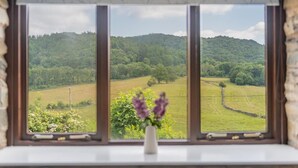 A window with a view of a green landscape, a vase with flowers, and a stone wall. - 2 Bed in Ulverston (oc-sz591) (Haverthwaite)