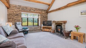 A cozy living room with a stone wall, a fireplace, a television, a sofa, and a window with a view of greenery. - 2 Bed in Ulverston (oc-sz591) (Haverthwaite)