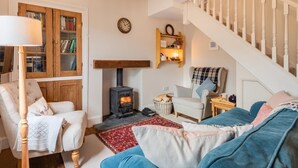 A cozy living room with a fireplace, a staircase, a bookshelf, and a comfortable seating area. - 3 Bed in Penrith (oc-sz184) (Glenridding)