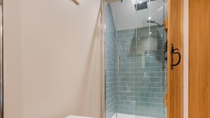 A bathroom with a glass shower enclosure, a white bench, and a wooden door. - 3 Bed in Penrith (oc-sz184) (Glenridding)