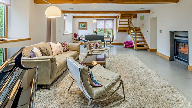 Ein geräumiger Wohnbereich mit Sofa, Sessel und Esstisch. Eine Treppe führt zu einer oberen Ebene.