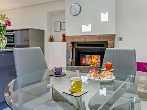 A modern living room with a glass table, two grey chairs, a fireplace, and a clock on the wall. - 4 Bed in Holmrook (oc-sz293) (Irton with Santon)