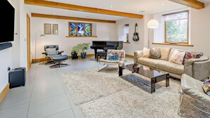Ein geräumiges Wohnzimmer mit Klavier, einer Couch, einem Fernseher und einem großen Fenster.