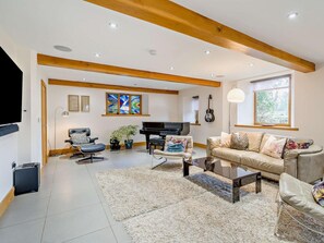 Ein geräumiges Wohnzimmer mit Klavier, einer Couch, einem Fernseher und einem großen Fenster.