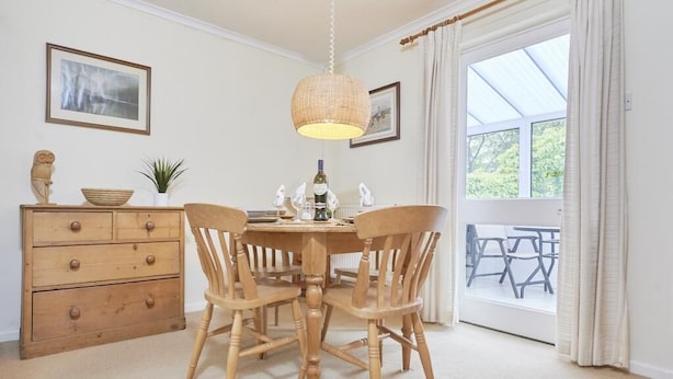 A dining area with a round table, wooden chairs, a hanging light fixture, and a view through a glass door to an outdoor seating area. - 2 Bed in Keswick (oc-sz188) (Keswick)