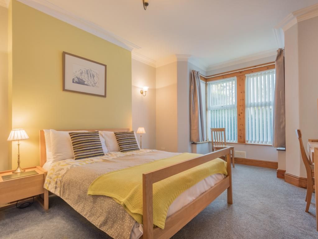 A bedroom with a bed, bedside tables, a window with curtains, and a wall-mounted picture.