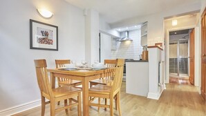 A dining area with a wooden table and chairs, a kitchen in the background, and a hallway leading to a door. - 2 Bed in Keswick (oc-sz019) (Keswick)