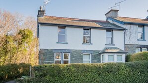 A two-story house with a stone facade, a tiled roof, and a well-maintained hedge in front. - 2 Bed in Keswick (oc-sz019) (Keswick)