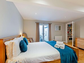 Ein Hotelzimmer mit Bett, Stuhl, Bücherregal und Blick durch eine Tür.