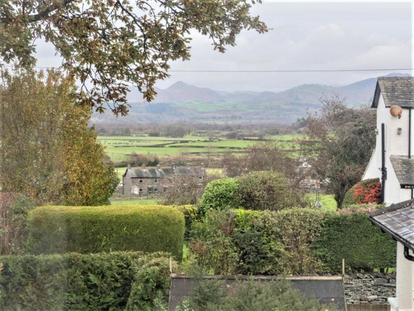 A rural landscape with a stone house, hedges, and distant mountains.