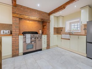 A kitchen with a brick wall, wooden beams, and cream-colored cabinets. - 4 Bed in Penrith (oc-sz321) (Hackthorpe)