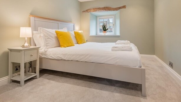 Quarto com cama, mesa de cabeceira, abajur e janela com uma planta.