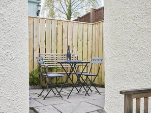 Ein Außenbereich mit Terrasse, Holzlattenzaun, Tisch und vier Stühlen.