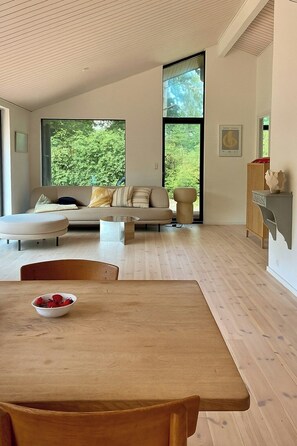 A modern living room with a sofa, a dining table, and a fireplace. - Beautiful cottage with a simple modern aesthetic (Vejby Strand)