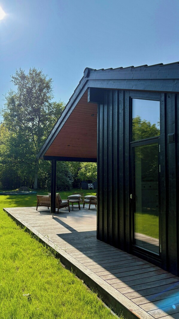 A modern outdoor structure with a wooden deck, seating area, and glass walls. - Beautiful cottage with a simple modern aesthetic (Vejby Strand)