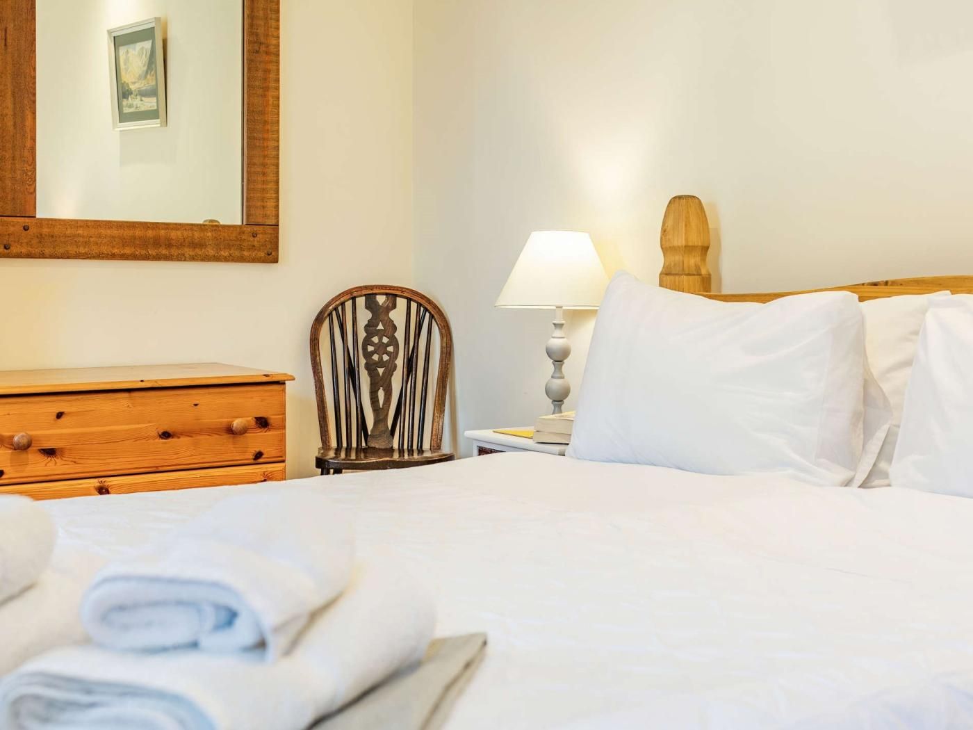 A hotel room with a bed, a wooden dresser, a chair, a lamp, and a mirror.