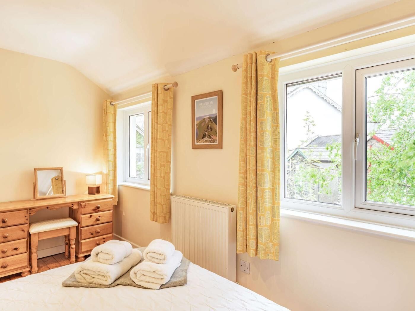 A bedroom with a bed, a dresser, a mirror, a window with curtains, and a radiator.