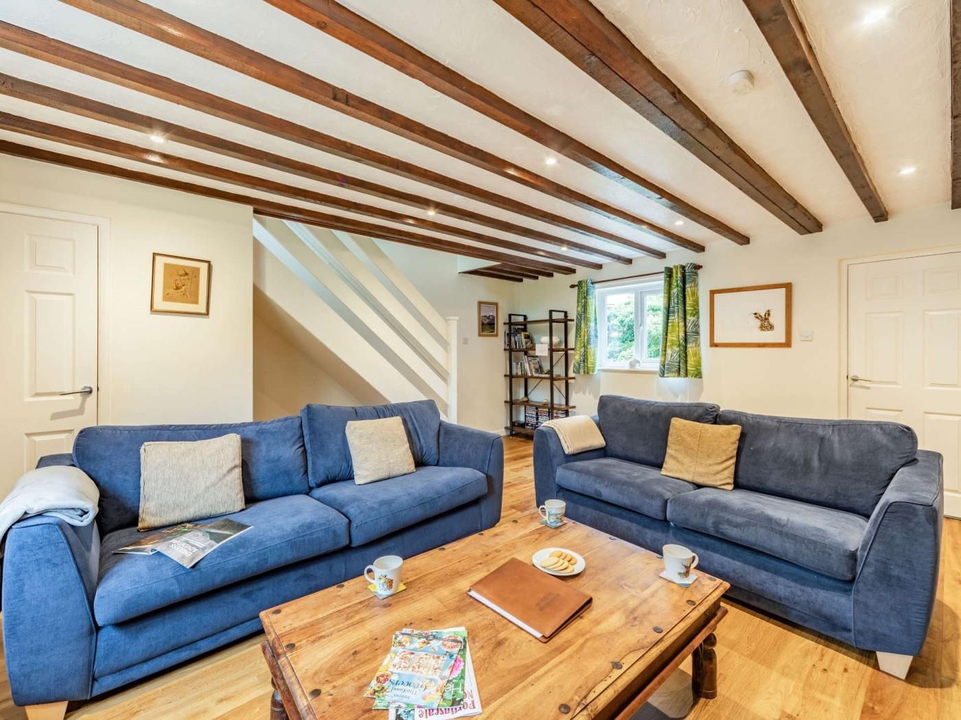 Une pièce avec deux canapés bleus, une table basse en bois et une bibliothèque.
