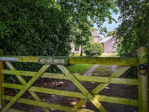 A wooden gate with a sign reading 'NETHER HOUSE' leading to a building with a stone facade. - 5 Bed in Ulverston (oc-sz587) (Broughton Beck)