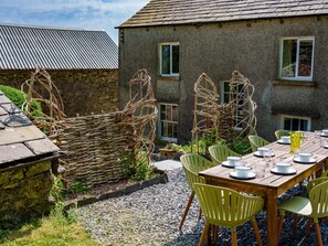 A rustic stone building with a thatched roof, a wooden table set for dining, and wicker baskets. - 5 Bed in Ulverston (oc-sz587) (Broughton Beck)