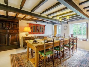 A dining area with a wooden table set for four, surrounded by chairs with green cushions, a patterned rug, and a wooden ceiling with exposed beams. - 5 Bed in Ulverston (oc-sz587) (Broughton Beck)