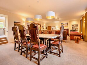 Uma sala de jantar com uma mesa grande, seis cadeiras de madeira com assentos de couro e três luminárias pendentes.