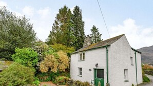 A white building with a green door, surrounded by greenery and a stone path. - 2 Bed in Keswick (oc-sz302) (Rosthwaite)